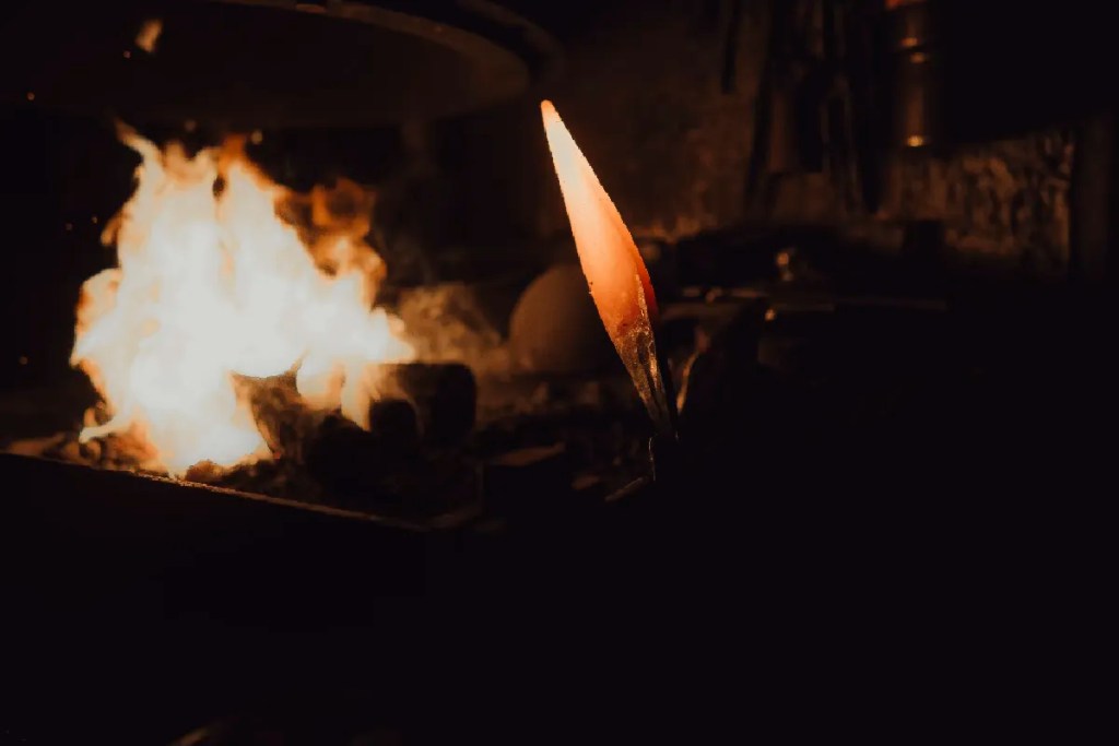 Glühende Metallspitze vor Feuer in einer Schmiede, Symbol für Transformation und Ursprung.
