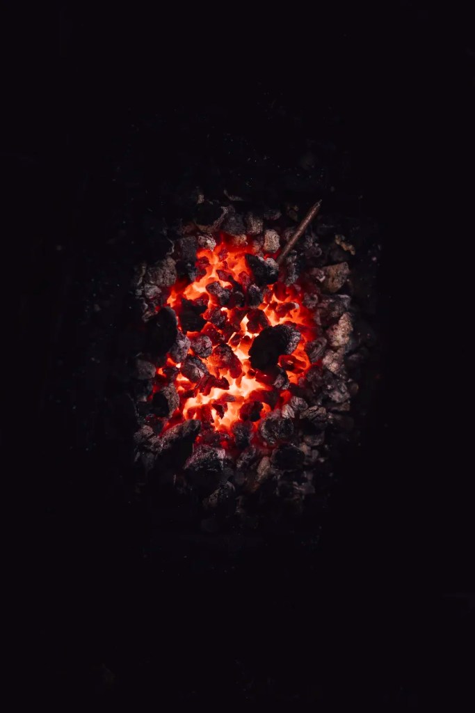 A glowing, heart-shaped forge hearth with burning charcoal, framed as the symbolic heart of the blacksmith’s forge.